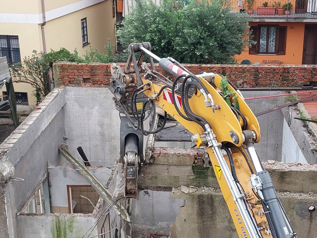 Demolizione fabbricato fatiscente e ripristino dell'area, macchinario dotato di frantumatore orientabile demolisce la parte alta della struttura in cemento di un fabbricato fatiscente